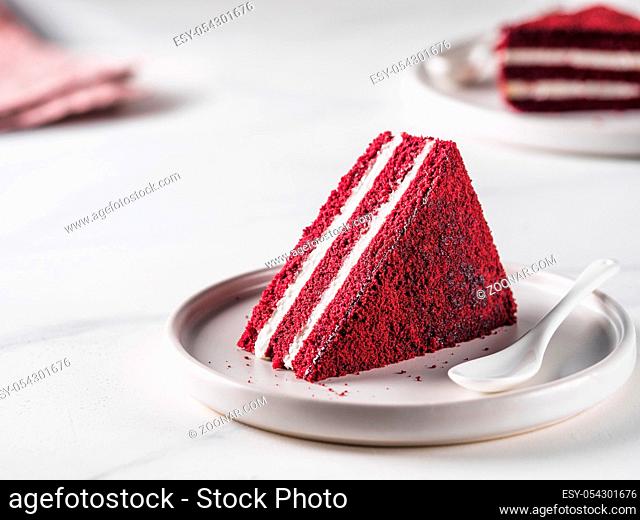 Piece of red velvet cake with perfect texture in matte plate on white marble tabletop. Slice of delicious homemade red velvet cake with raspberry and chocolate