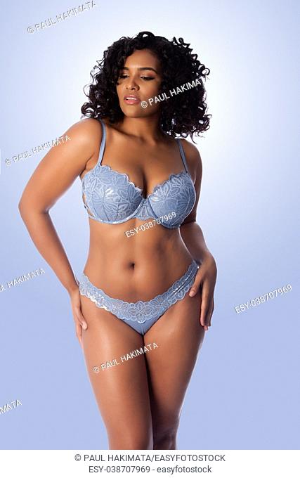 Beautiful happy plus size sexy woman with curly hair in light blue lingerie bra and thong underwear