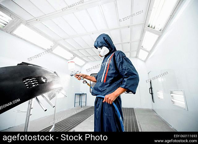 worker painting a car black blank parts in special garage, wearing costume and protective gear