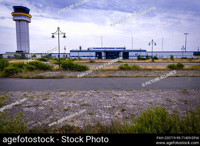 18 July 2022, Mecklenburg-Western Pomerania, Parchim: The terminal building stands behind a partially overgrown parking lot at the former airport