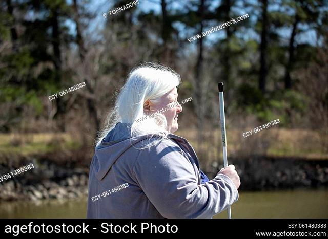 Albino woman holding her cane near water outdoors