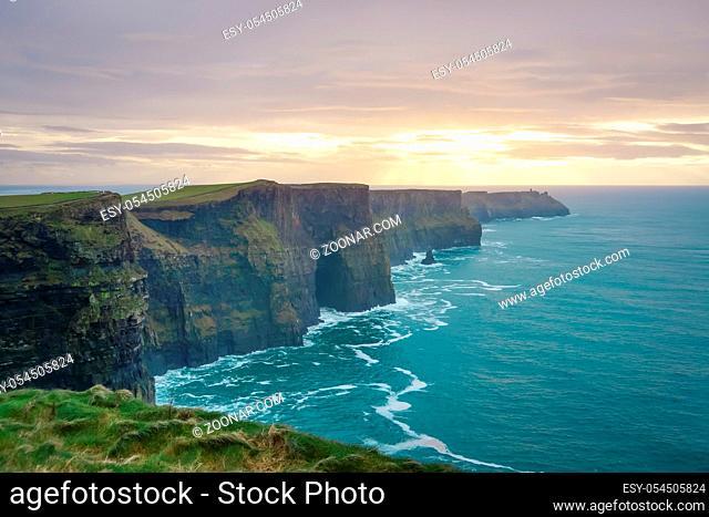 Iconic Cliffs of Moher in Wild Atlantic Way with beautiful dramatic sunset and waves on turquoise ocean