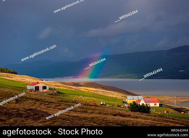 rainbow expanding over a wide river in a valley with a small white and red farm building on Iceland