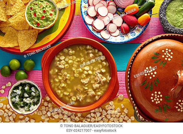 Green Pozole verde with blanco mote corn and ingredients on colorful table