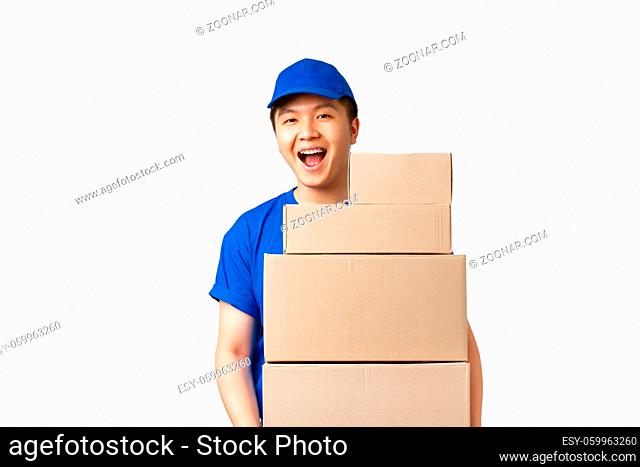 Online shopping, fast shipping concept. Upbeat smiling asian delivery man in blue courier uniform holding boxes with orders, carry parcels to client house