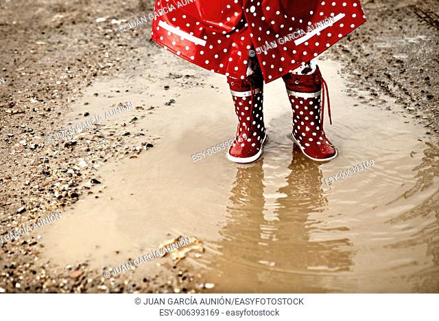 Detail of rainboots of a baby girl dressed with dotted raincoat in the puddles