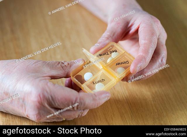 Closeup of an elderly senior woman's hands taking her medication for the week in a pill box on wooden table, business, health concept close up