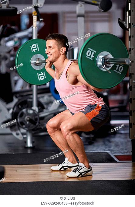 Athletic man doing squats with barbell on neck
