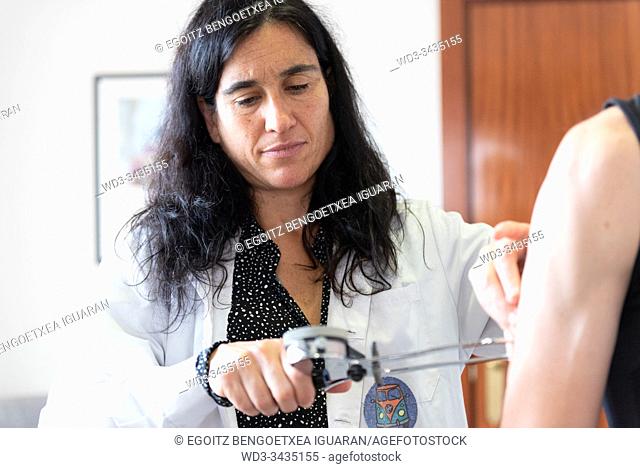 A female nutritionist measuring the body fat ratio of an athletic man by using a caliper. Plicometer