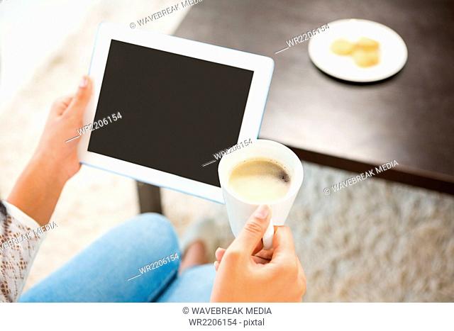 Smiling casual woman using her tablet while holding coffee