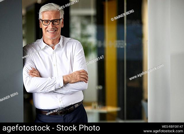 Businessman with arms crossed leaning on wall in office