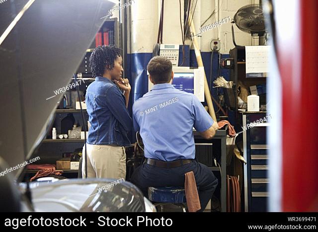 Mechanic and customer look at computer screen in auto repair shop