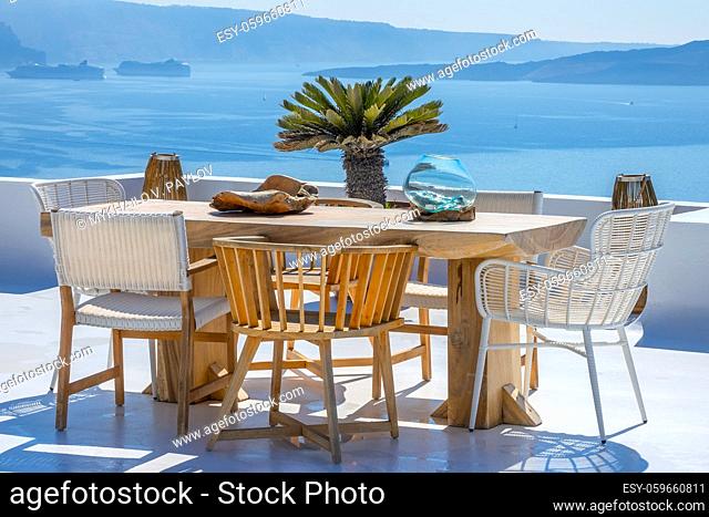 Greece. Santorini. Thira island. Wooden table and chairs on a sun terrace. Two cruise ships in the harbor