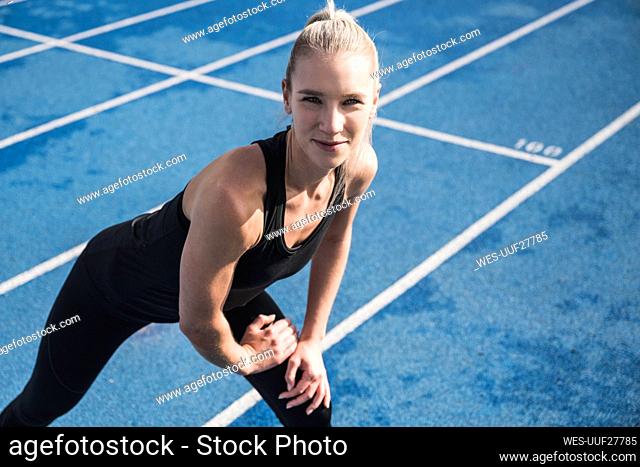 Smiling young sportswoman doing warm up exercise on track