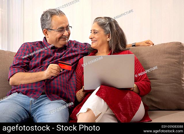 AN OLD COUPLE HAPPILY LOOKING AT EACH OTHER WHILE DOING ONLINE TRANSACTION