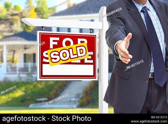Male agent reaching for hand shake in front of sold for sale sign and house
