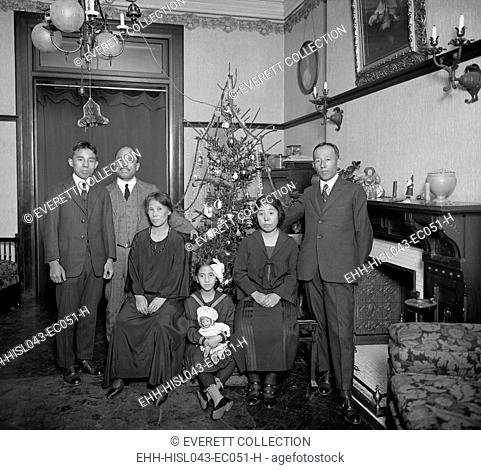 East Asian family with Christmas tree in their home in Washington, D.C. in 1921-22. The well-dressed group are in a spacious nicely furnished apartment...