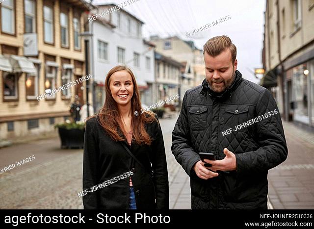 Man and woman standing in street and checking phone