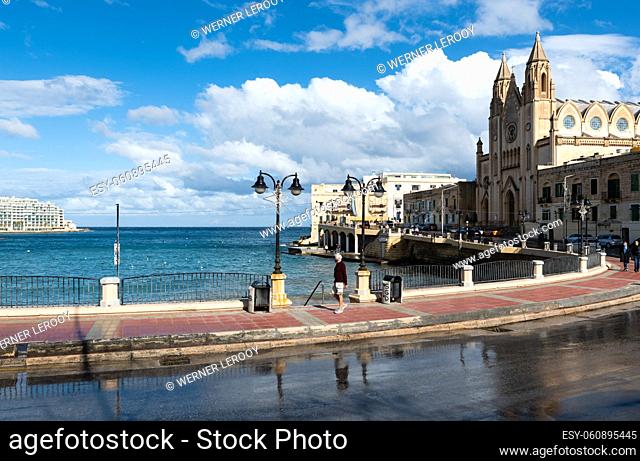 San Julian, Malta: View over the bay and the wet reflecting road with a tourist walking by