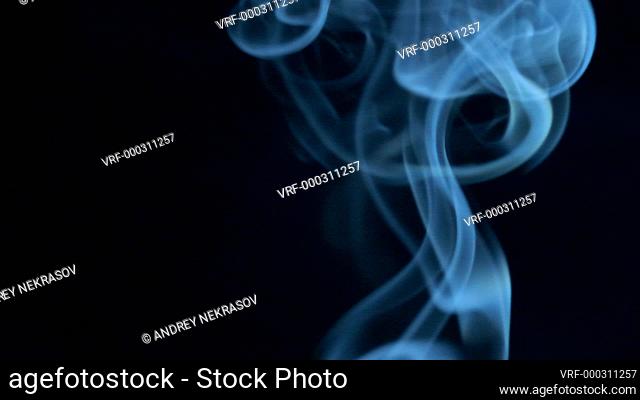 Blue smoke slowly rising graceful twists on black background blowing from bottom to top. Slow motion, Closeup