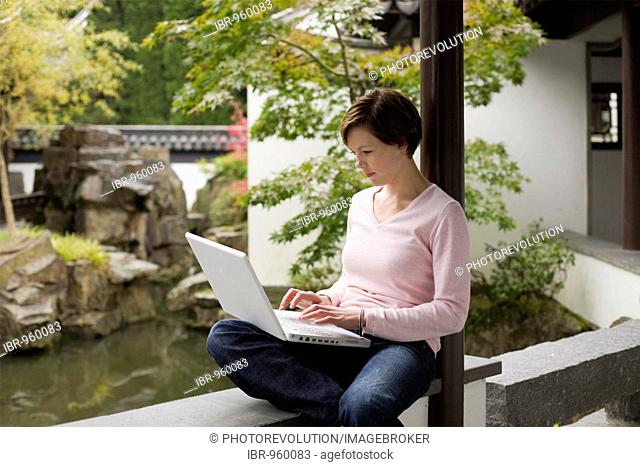 Young woman, student working on a laptop in a Chinese garden