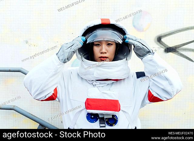 Female astronaut holding helmet while standing by wall