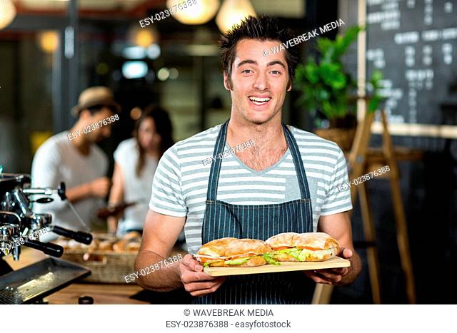 Smiling barista holding sandwiches