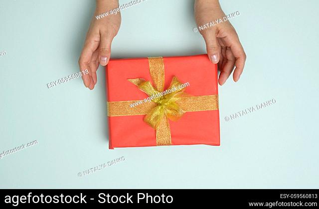 female hands are holding red gift box on a blue background, concept of congratulations on birthday, top view