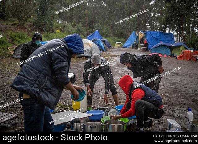 28 February 2021, Spain, San Cristobal de La Laguna: Men wash dishes and pots in heavy rain. Several people have decided to leave the refugee camp Las Raices to...