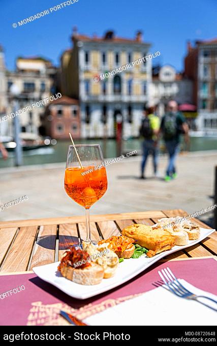 Glass with Spritz aperitif and Cicchetti dish, typical Venetian appetizers based on fish or cured meats served on a slice of bread or polenta