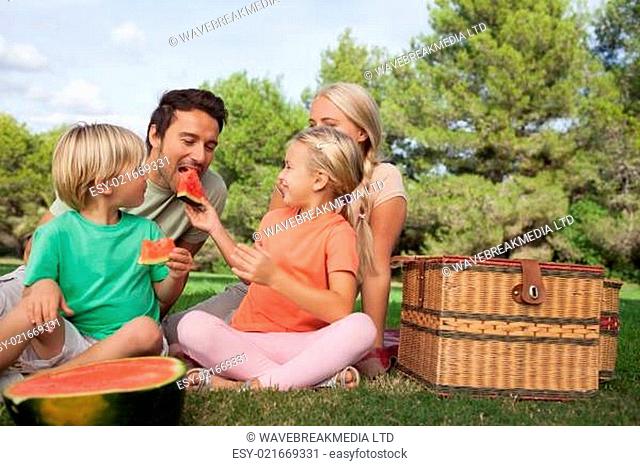 Happy family having a picnic and eating watermelon sitting in the park