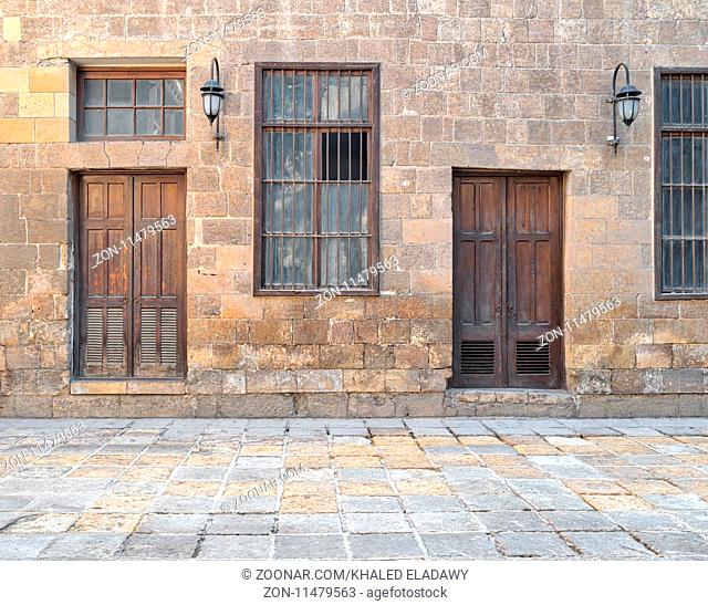 Facade of old abandoned stone bricks wall with wooden doors , windows covered with iron bars and lanterns, Cairo, Egypt