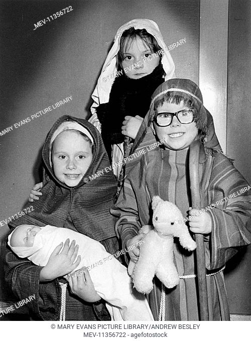 Three children taking part in a nativity play for Christmas, with a doll and a toy lamb