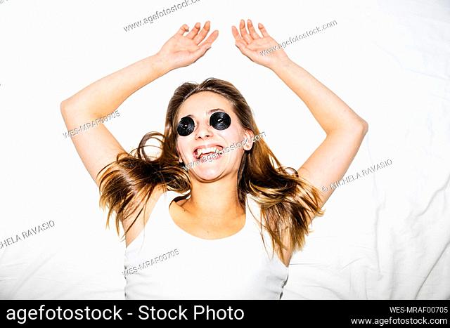 Cheerful young woman with eyes covered by licorice candies lying on bed