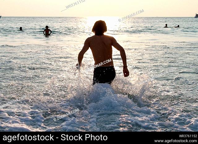 running man in water of tropical sea and splashing water. Vacations on sea shore