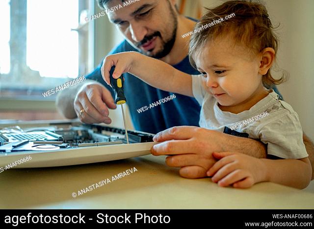 Boy helping father in repairing computer on table at home