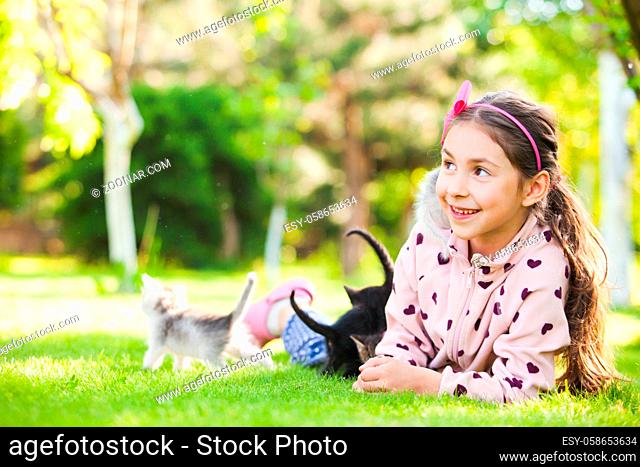 Outdoor portrait of cute girl playing with small kittens on natural background