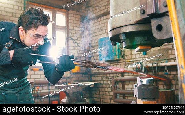 Man blacksmith in workshop forging red hot iron on anvil - small business, telephoto