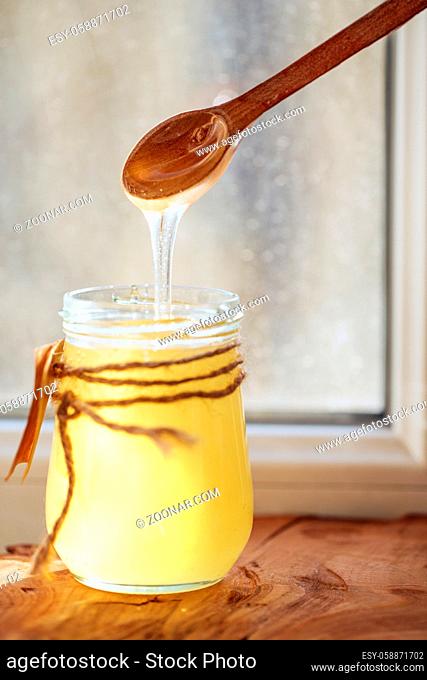 Honey dripping from a wooden spoon against window