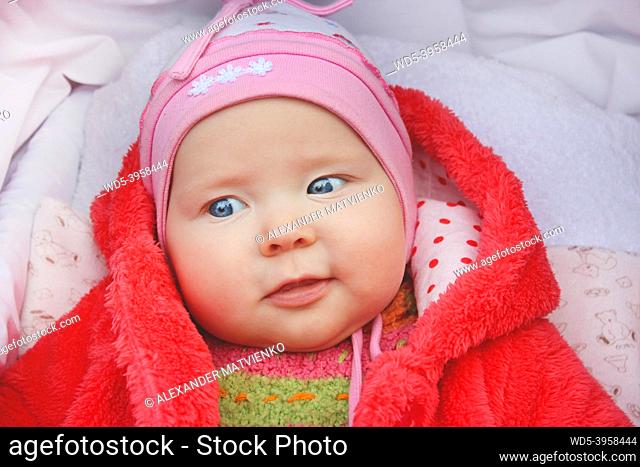 little baby in red suit smiling in perambulator. Happy baby laying in pram. Childish face close up