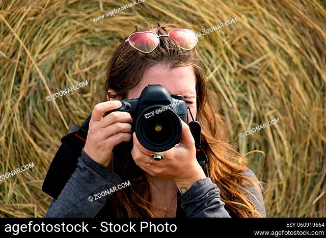 Female photographer with a digital reflex taking a shot towards the camera with a big bale of dry hay in the background. Outdoor rural shooting