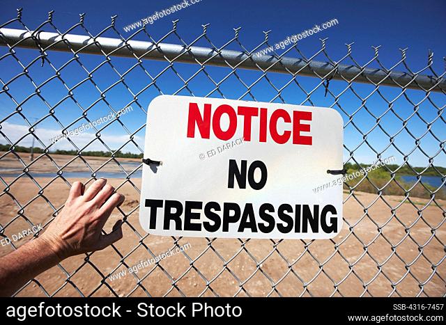 Man's hand clawing at fence with No Trespassing sign