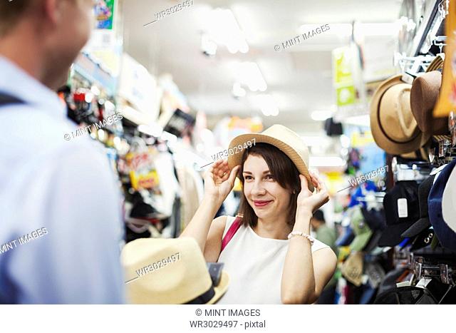 Smiling woman with brown hair stanching in a clothing store, trying on Panama hat