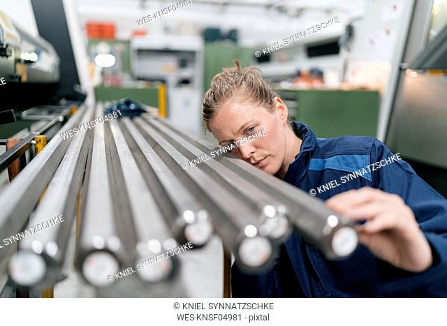 Young woman working as a skilled worker in a high tech company, checking steel rods