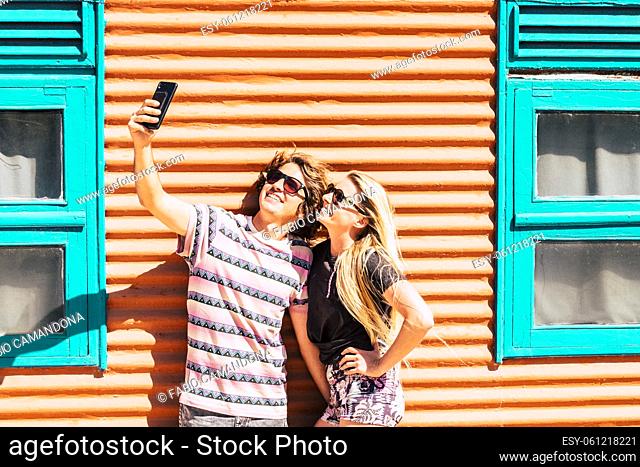 Young modern cheerful couple man and woman take together a selfie picture in outdoor wirh colorful orange and blue wall in background - beautiful and youthful...
