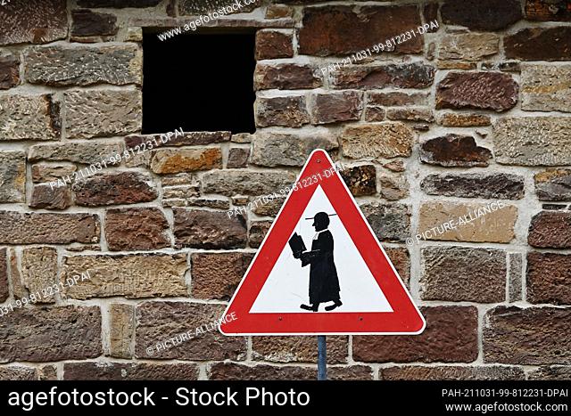 30 October 2021, Lower Saxony, Schönhagen: A symbolic road sign with a pilgrim stands in front of a stone wall at the Martin Luther Church in Solling