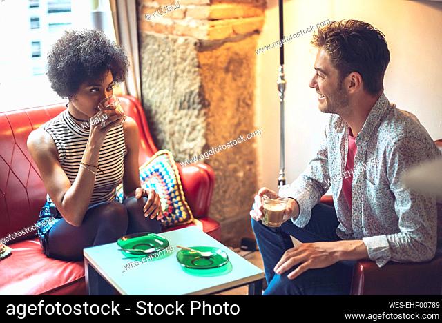Smiling man looking at girlfriend drinking coffee while sitting in cafe