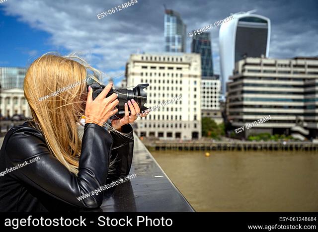 Female tourist photographing London city from the London Bridge towards the Tower Bridge and the business district. London, United Kingdom