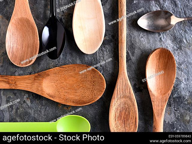 An assortment of wood, plastic, and metal spoons on a slate surface. Top view in horizontal format