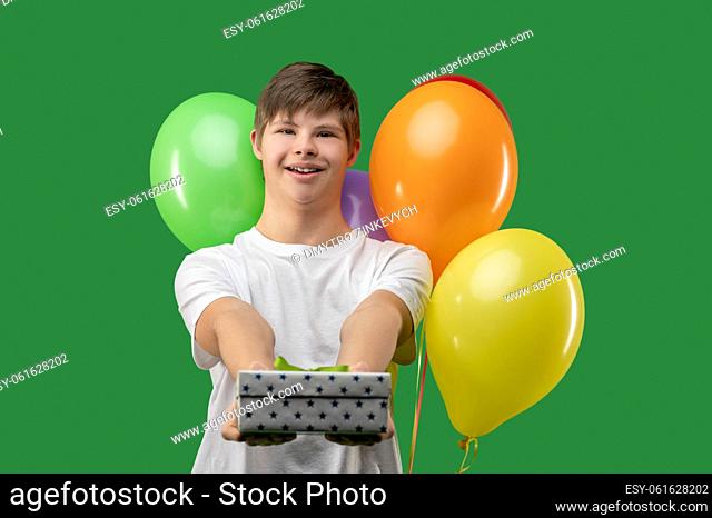 Waist-up portrait of a happy birthday boy holding a present box in front of the camera